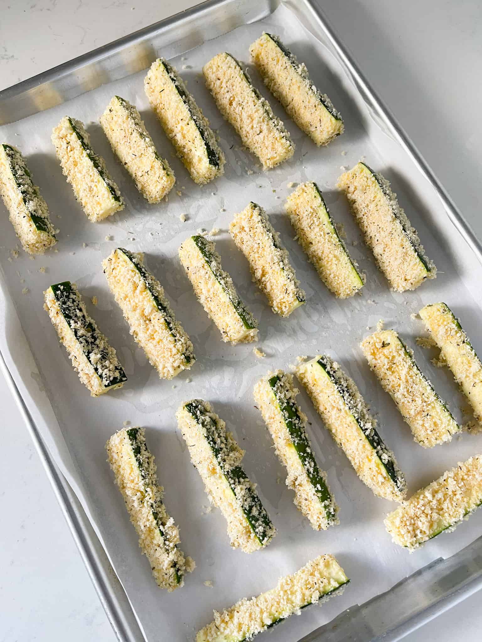 Zucchini fries lined on a baking sheet.