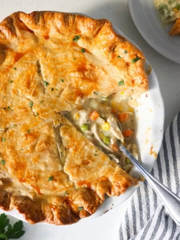 Overhead view of chicken pot pie in a white pie dish with a section cut out.