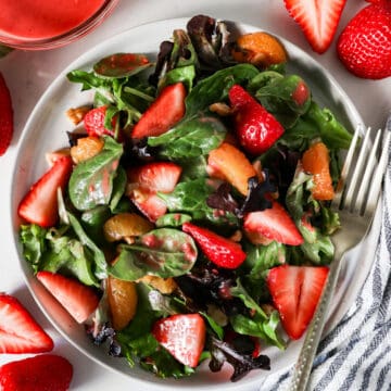 Overhead view of strawberry salad on a serving plate with raspberry vinaigrette dressing drizzled on top.