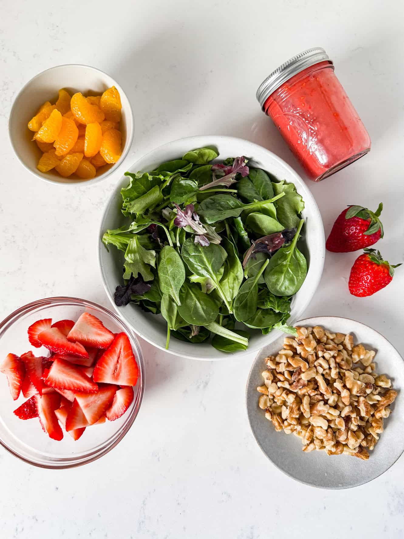 Strawberry salad ingredients spread out on a white countertop.