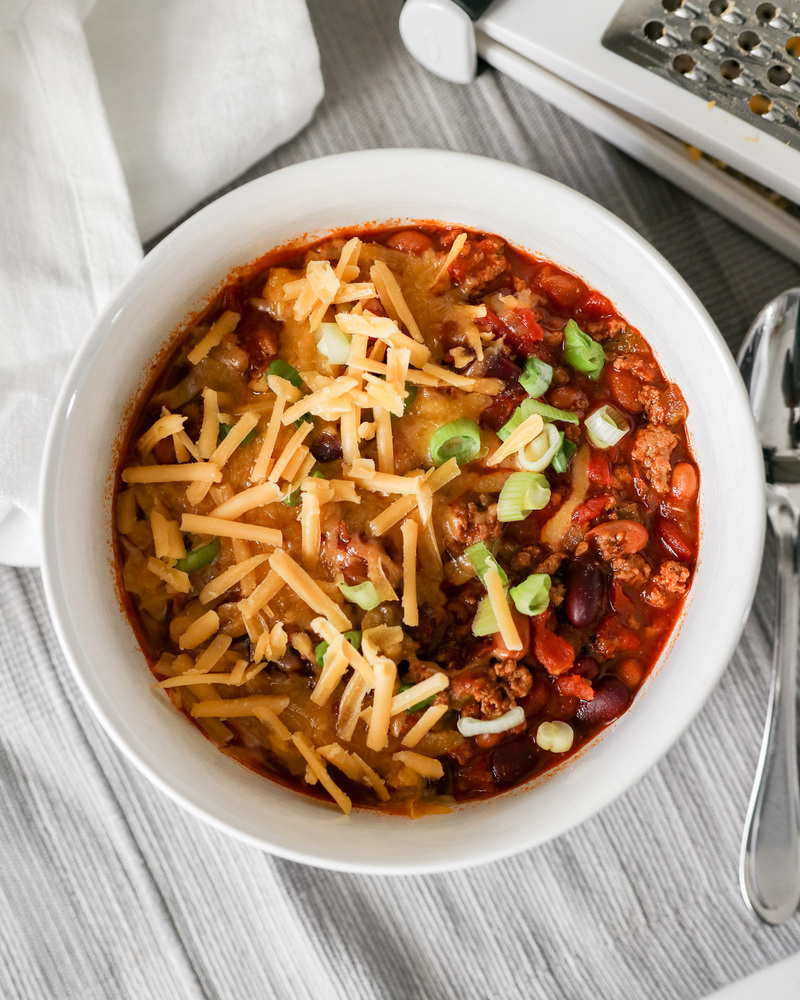 Overhead view of a bowl full of Instant Pot Chili with sliced onions and shredded cheese on top.