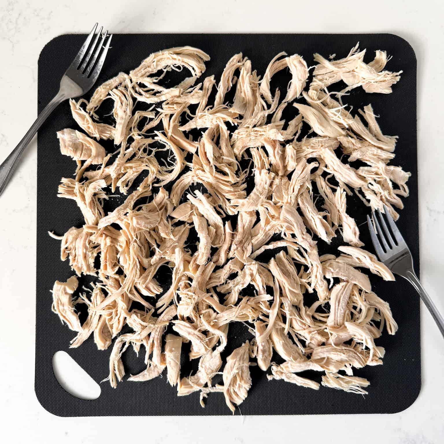 Shredded chicken breasts on a cutting board.