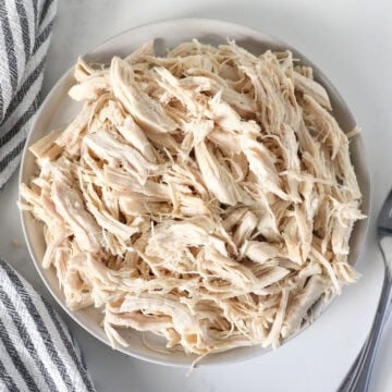 Overhead view of boiled and shredded chicken breasts on a plate with a napkin on the side.