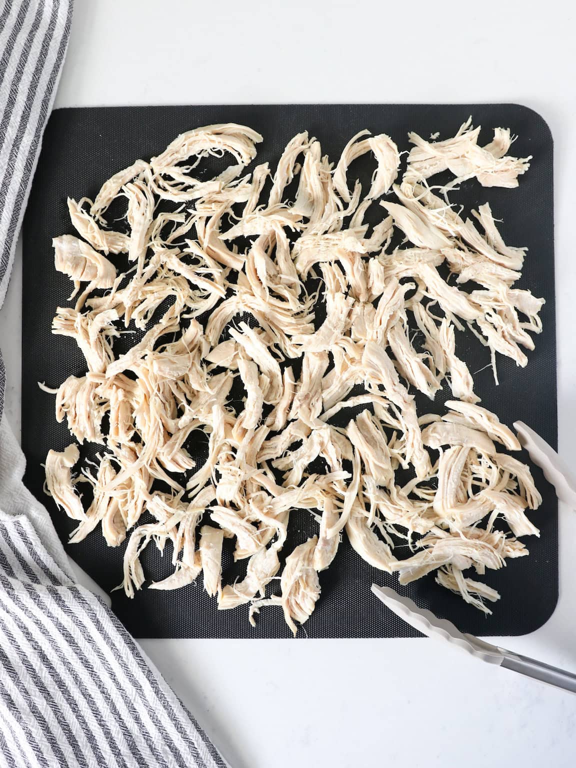 Overhead view of shredded chicken breasts on a cutting board with a napkin on the side.