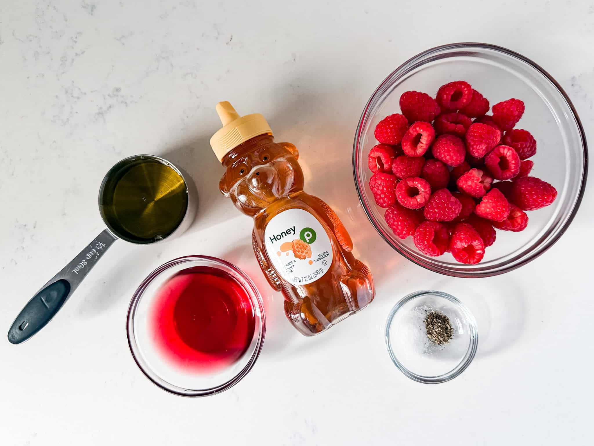 Ingredients for raspberry vinaigrette dressing spread out on white countertop.