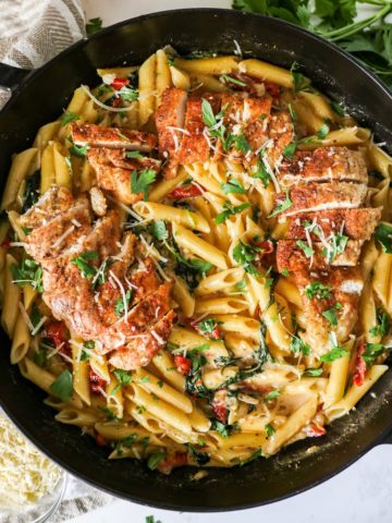Tuscan Chicken Pasta with sun-dried tomatoes in a cast iron skillet garnished with parsley and parmesan cheese.