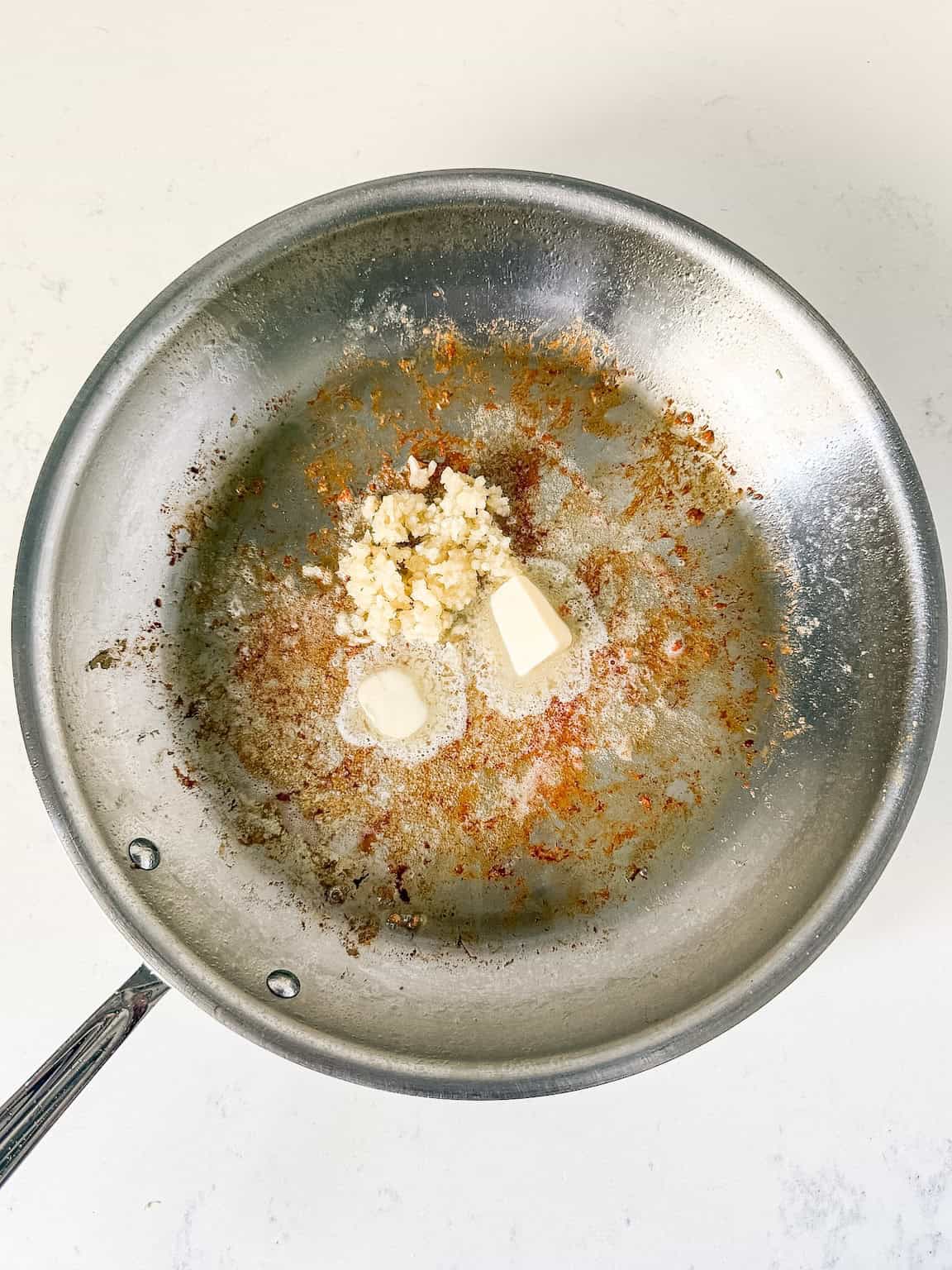 Garlic being sautéed in butter in a skillet.