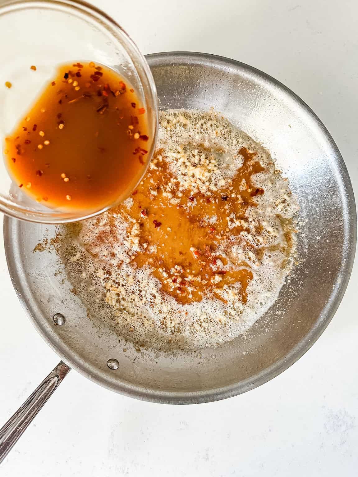 Honey sauce being pour in skillet with butter and garlic.