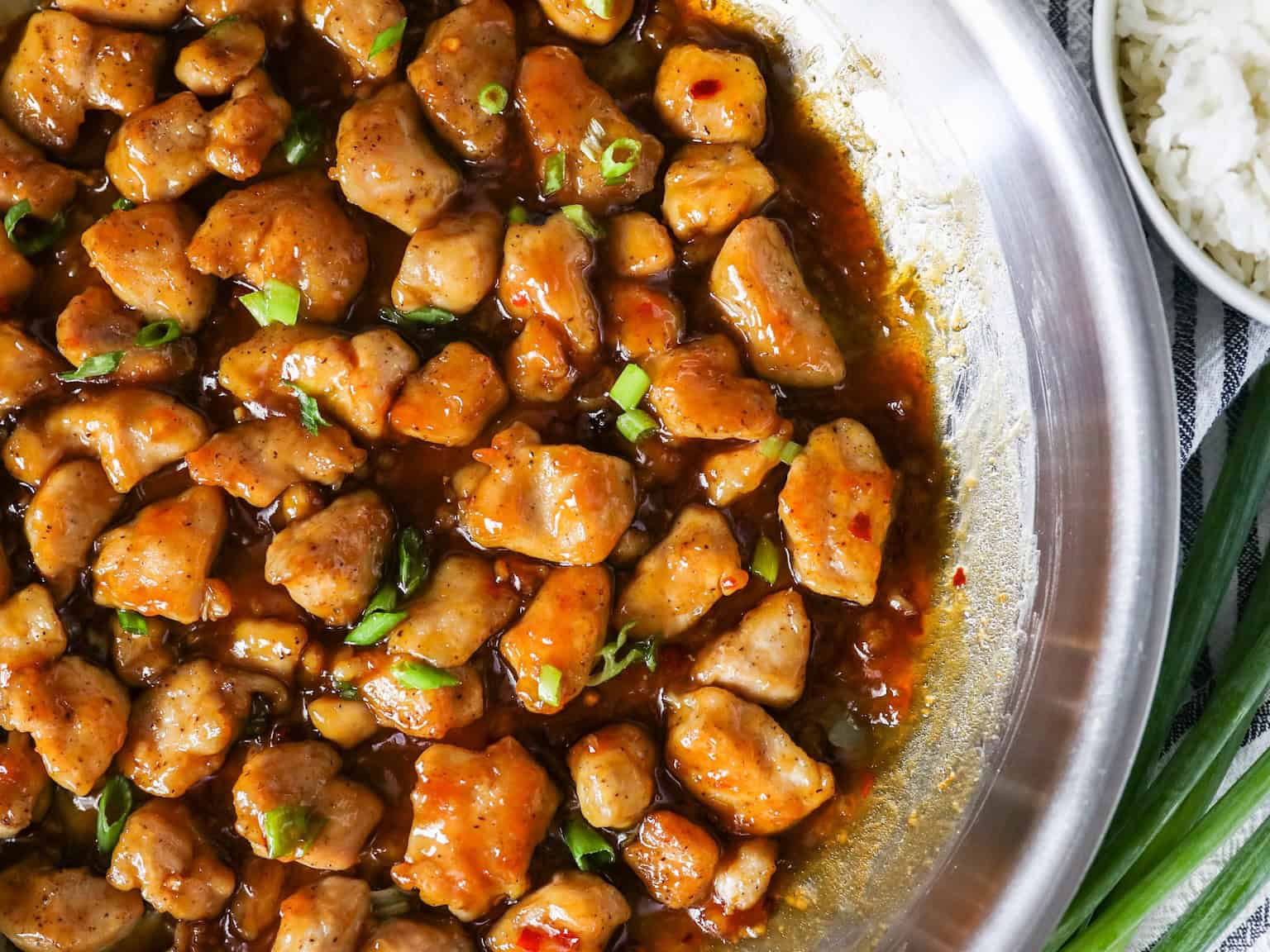 Overhead view of honey garlic chicken in a large stainless steel skillet.