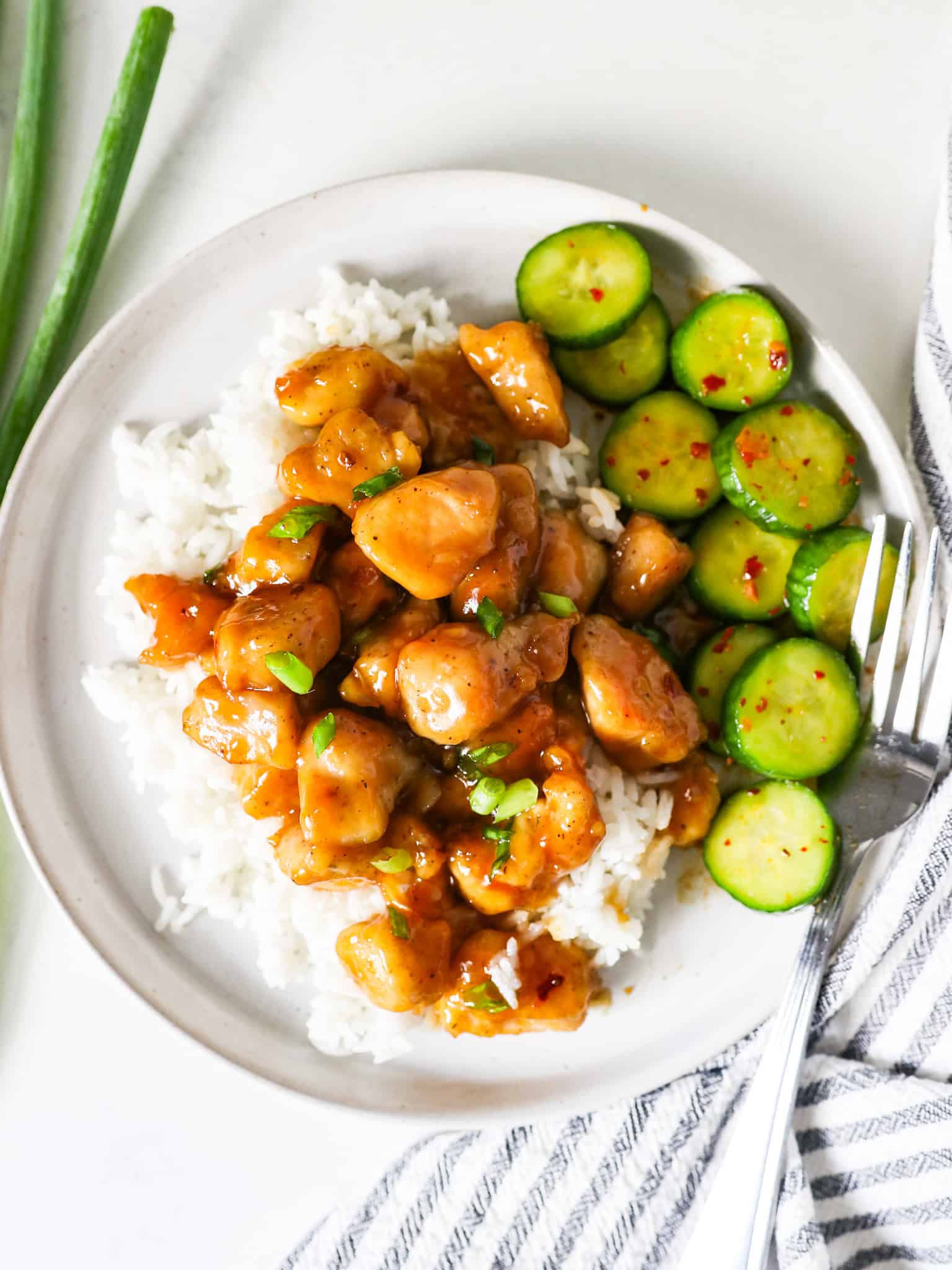 Overhead view of honey garlic chicken served on a bed of rice, on a white plate, with a side of cucumber salad.
