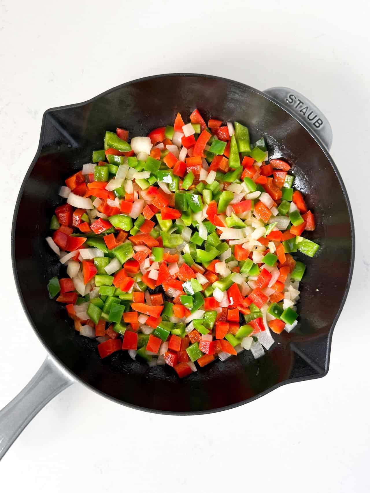 Bell peppers and onions being sautéed in a skillet.