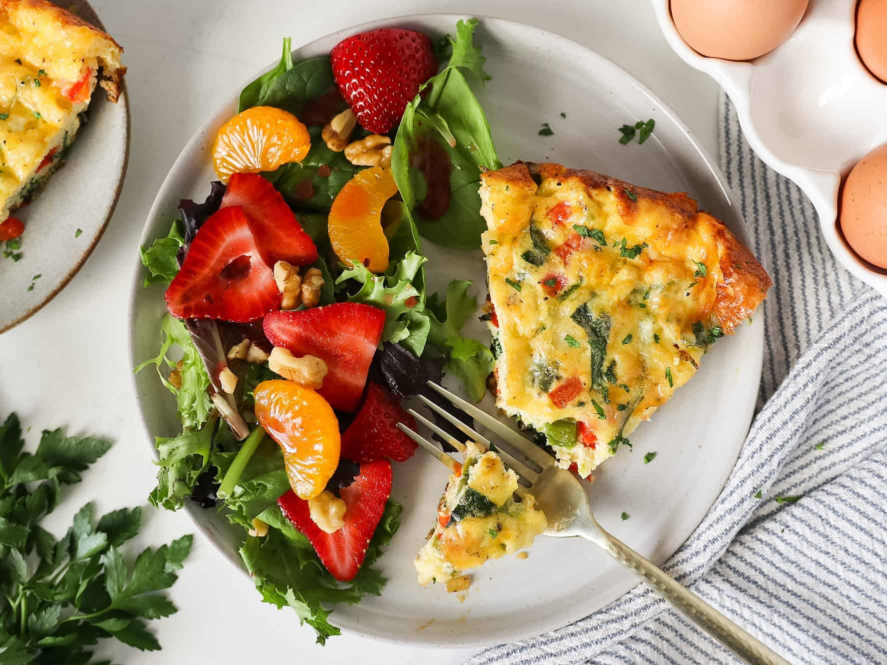 Overhead view of a slice of a frittata on a serving plate with a side of strawberry spring salad.