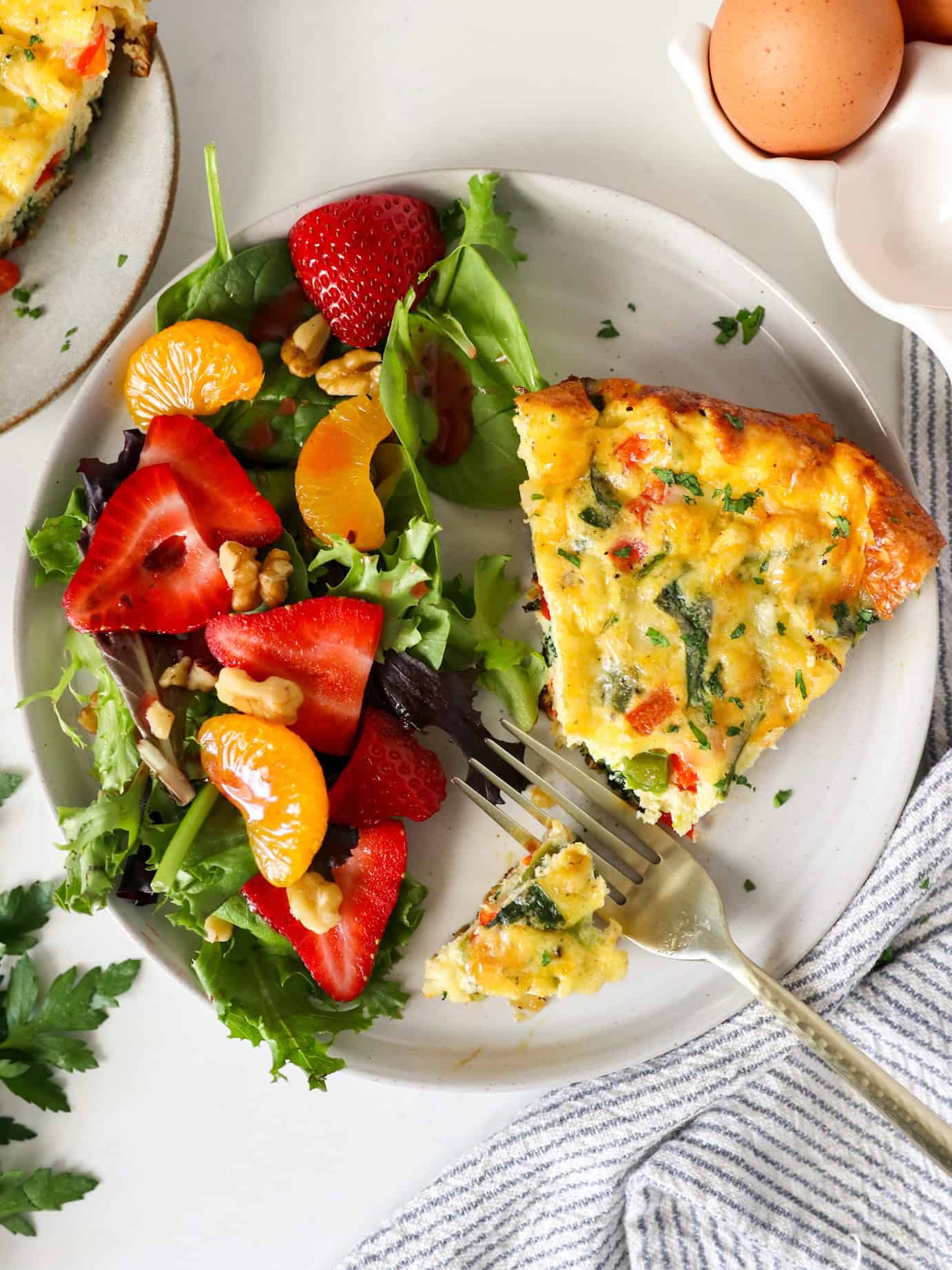 Overhead view of a slice of a frittata on a serving plate with a side of strawberry spring salad.