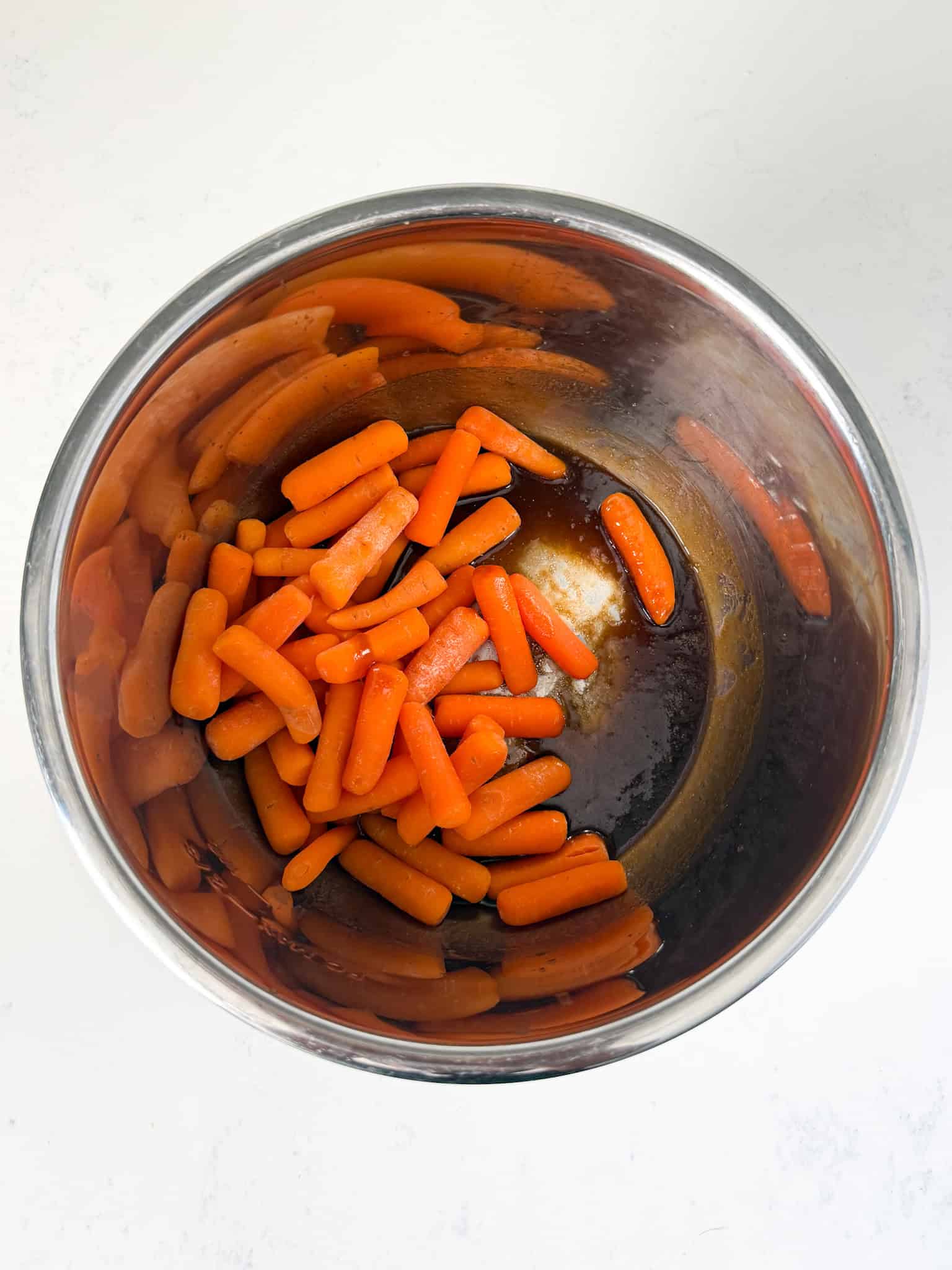 Cooked carrots being added to sugar glaze inside the instant pot.