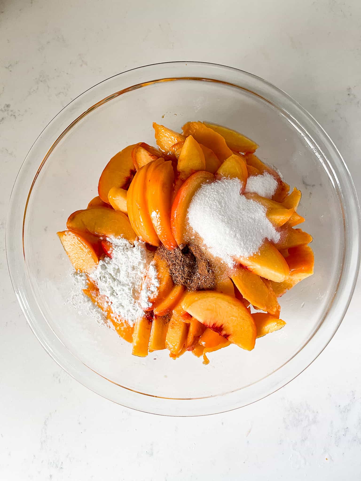 Sliced peaches in a bowl with sugar and spices on top.