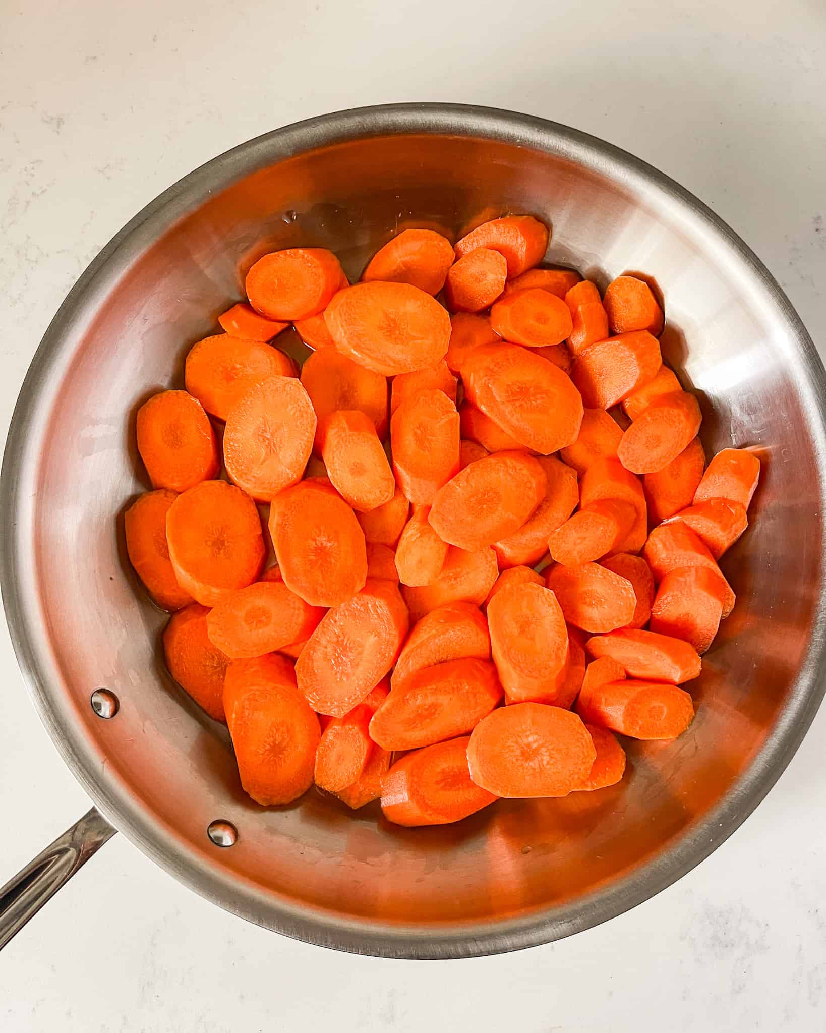 Sliced carrots in a skillet with water.