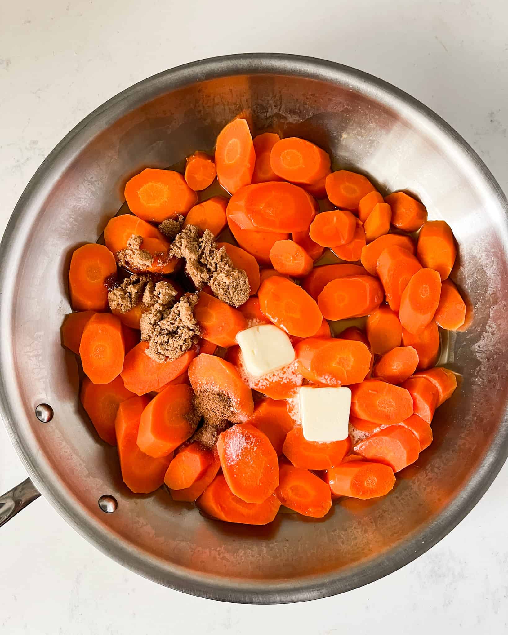 Sliced carrots in a skillet with butter, brown sugar, maple syrup, salt, and cinnamon.