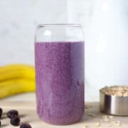 Front view of a blueberry oatmeal smoothie in a clear glass.
