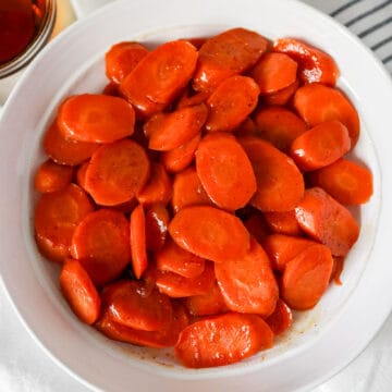 Overhead view of glazed carrots in a white serving dish with a white napkin on the side.