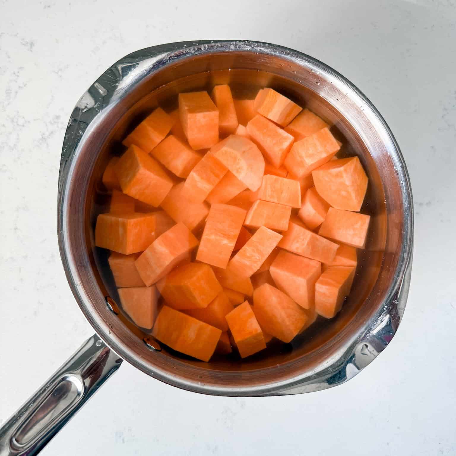 Chopped sweet potatoes boiling in a pot of water.