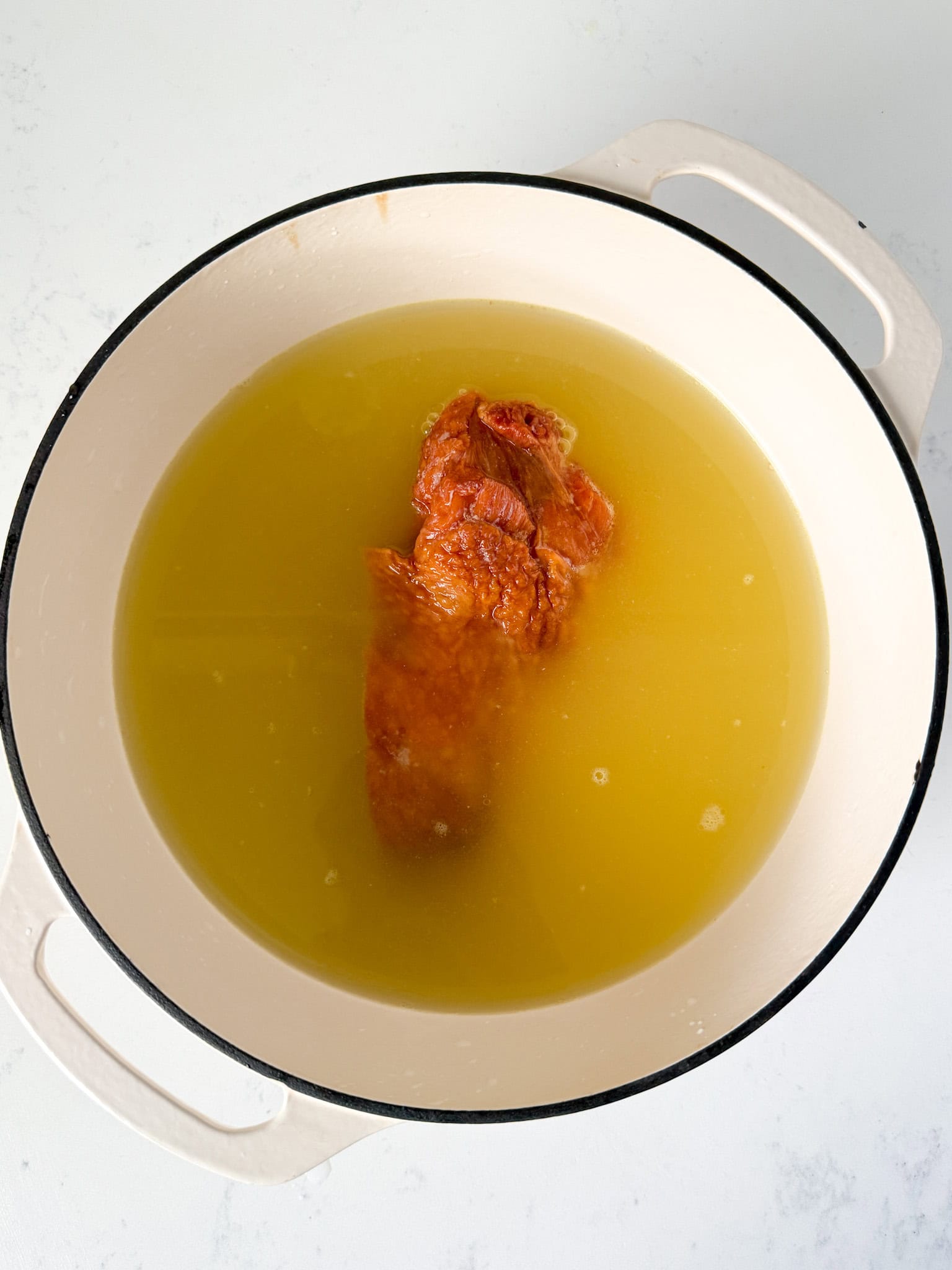 Smoked turkey wing in a white dutch oven with chicken broth and water.