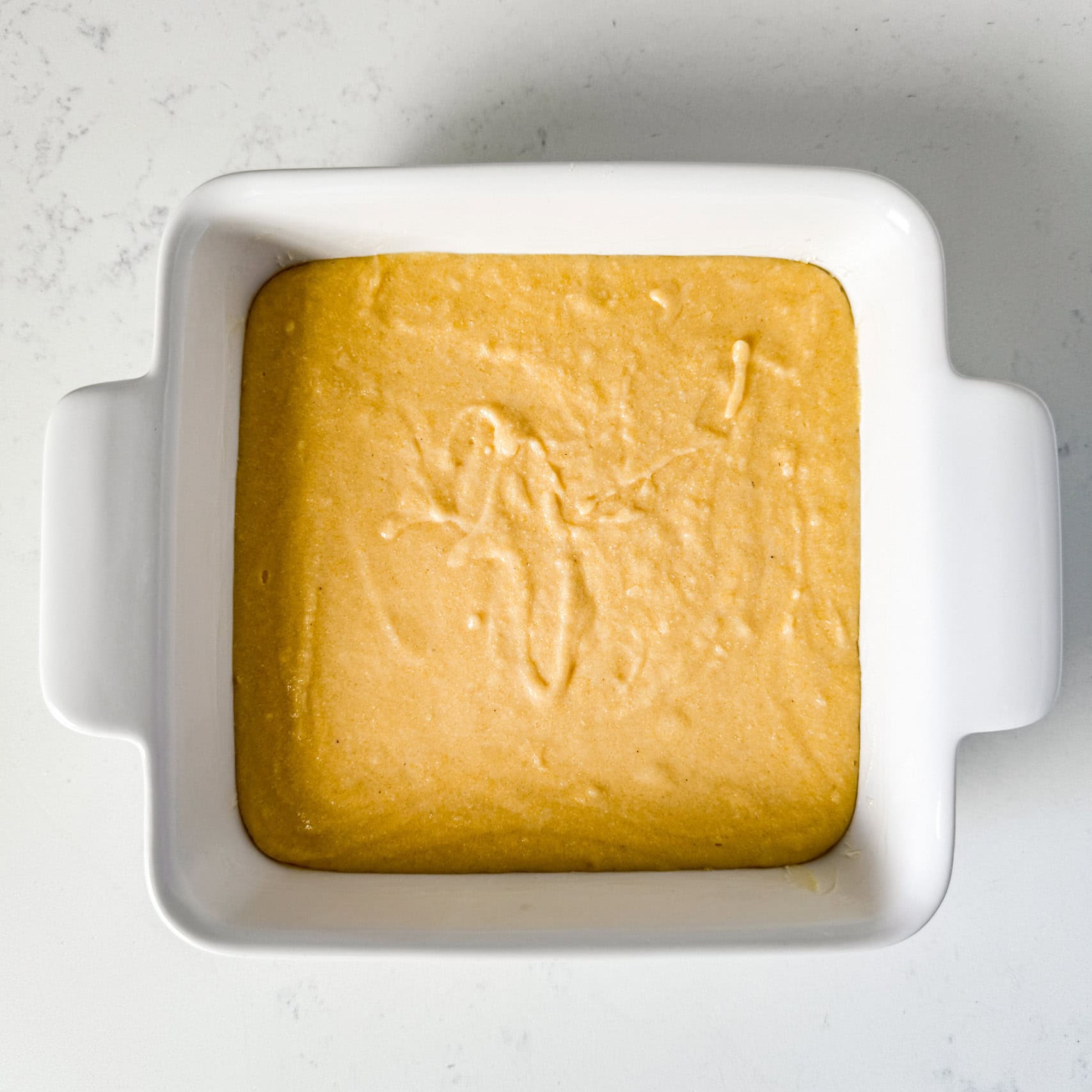 Cornbread batter spread out in a white baking dish.