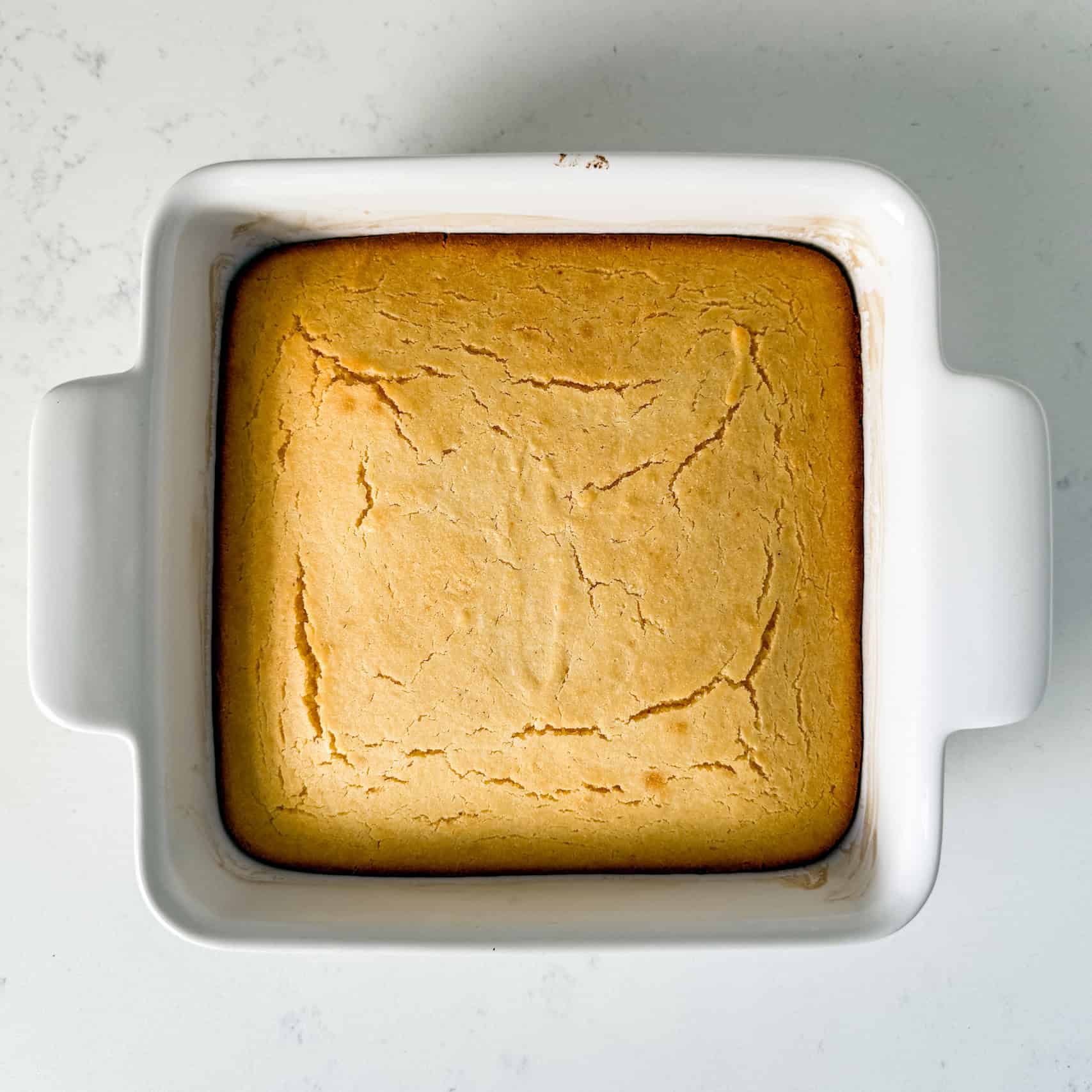Cooked homemade cornbread in a white baking dish.