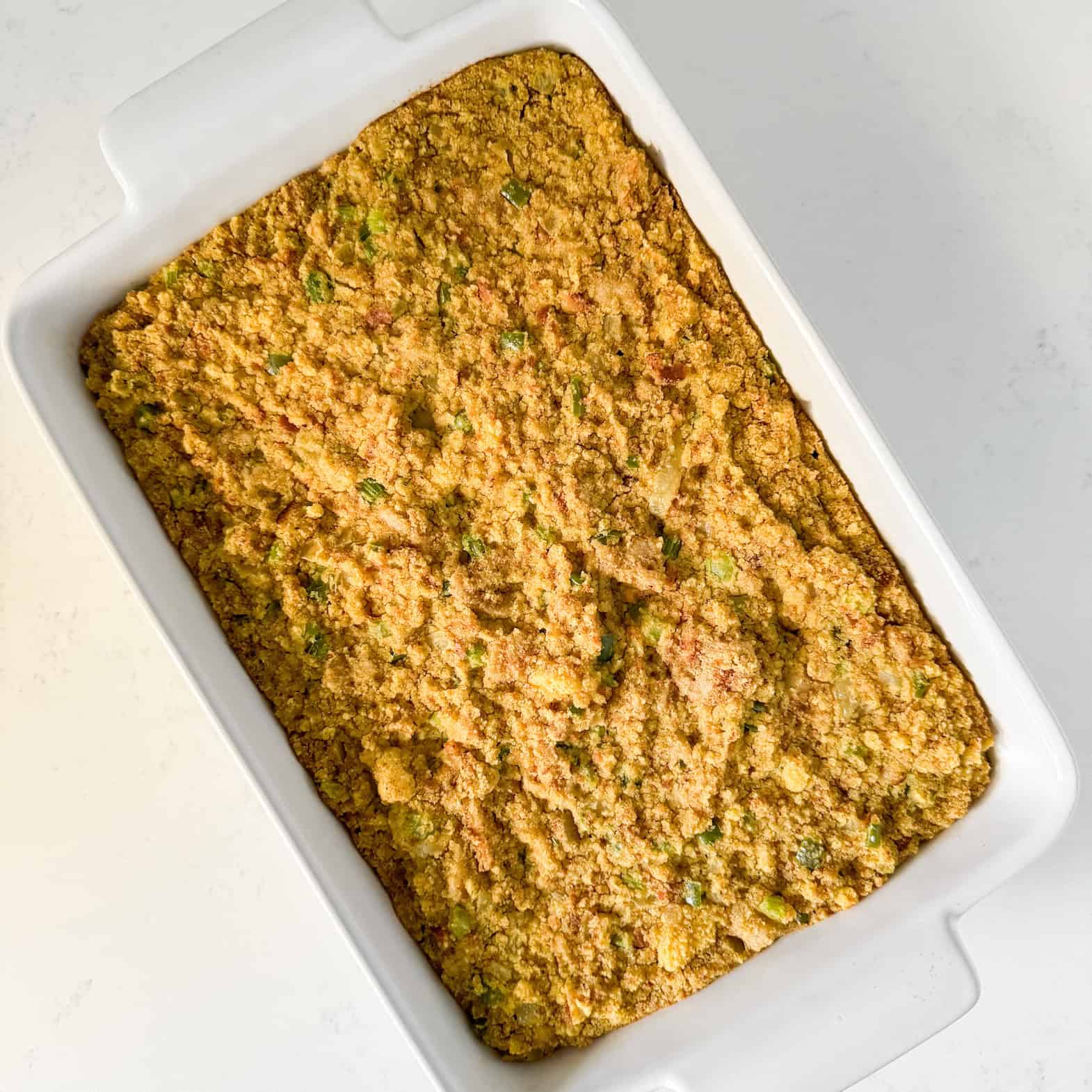 Cooked cornbread dressing in a white baking dish.