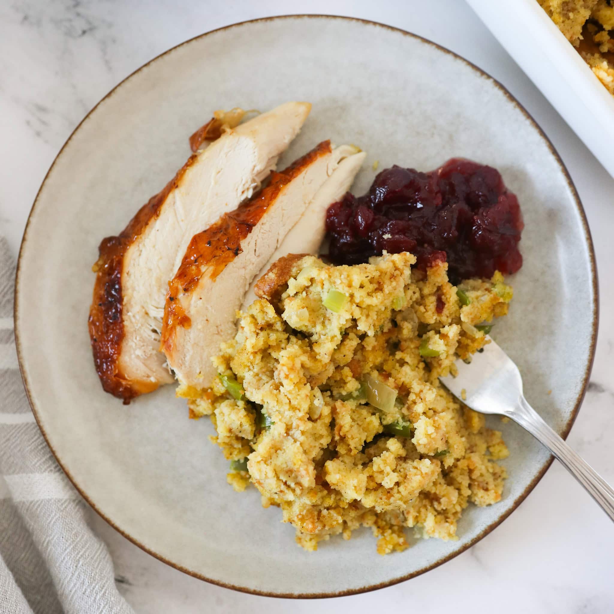 A serving of cornbread dressing on a plate with roasted chicken and cranberry sauce.