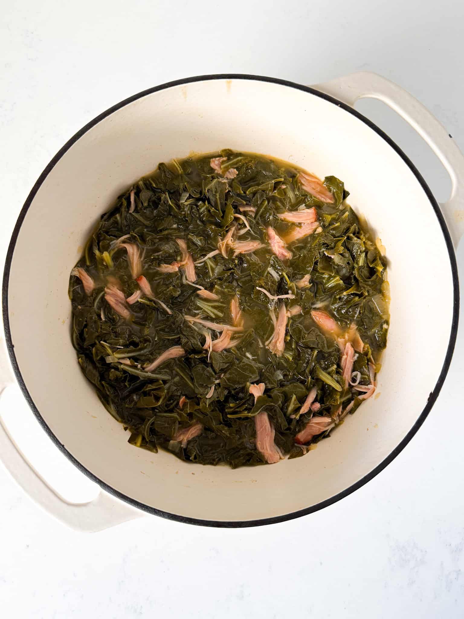 Cooked collard greens with smoked turkey in a dutch oven.