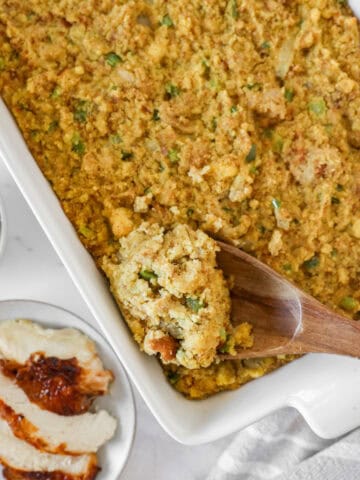Overhead view of cornbread dressing in a white casserole dish with a wooden spoon scooping some out.