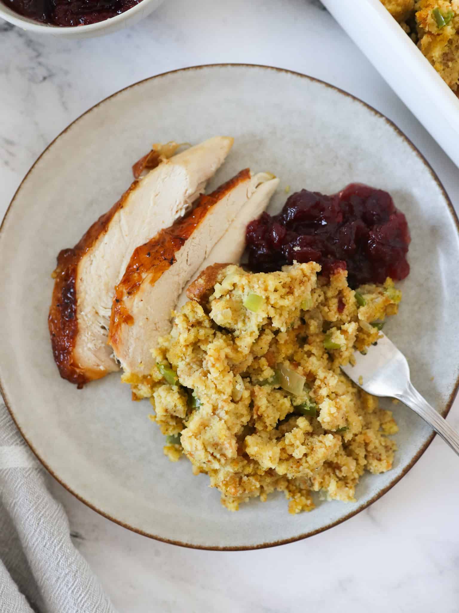A serving of cornbread dressing on a plate with roasted chicken and cranberry sauce.