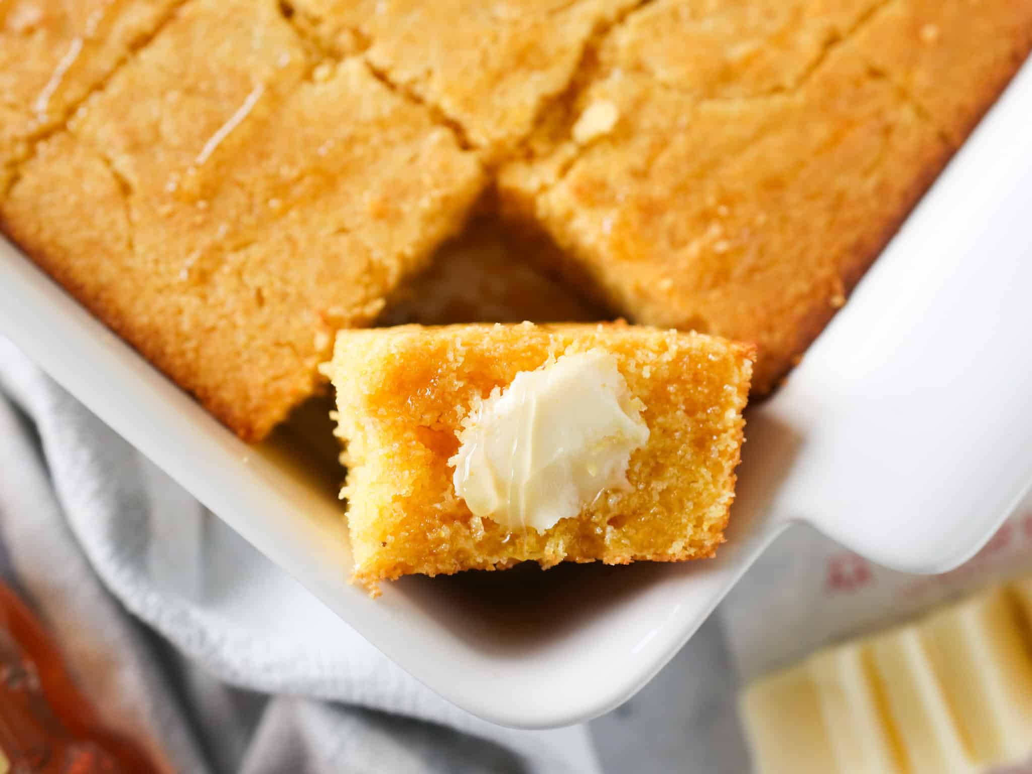 Overhead view of homemade cornbread with one slice turned on its side and butter and honey added on top.