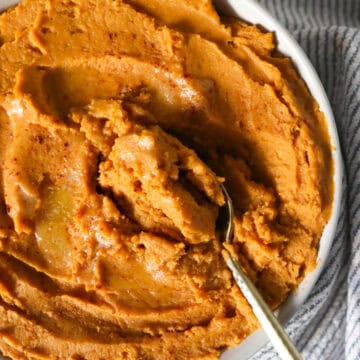 Overhead view of creamy mashed sweet potatoes in a serving dish with a spoon scooping some out.