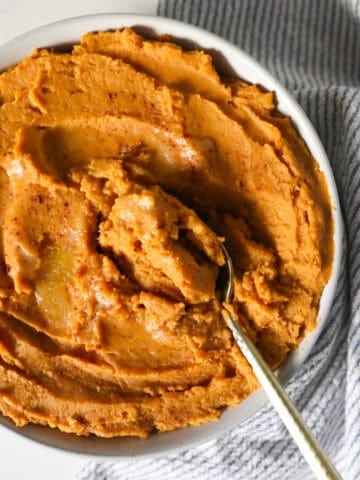 Overhead view of creamy mashed sweet potatoes in a serving dish with a spoon scooping some out.