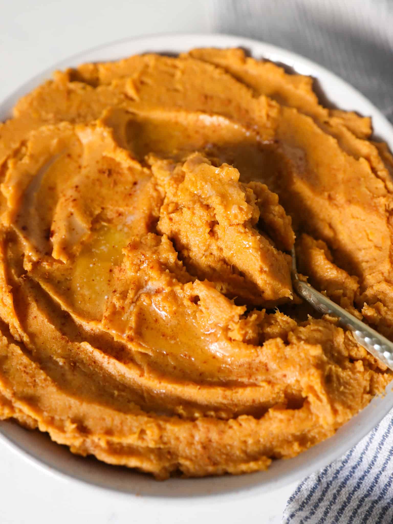 Side close up view of creamy mashed sweet potatoes with a spoon scooping some out.