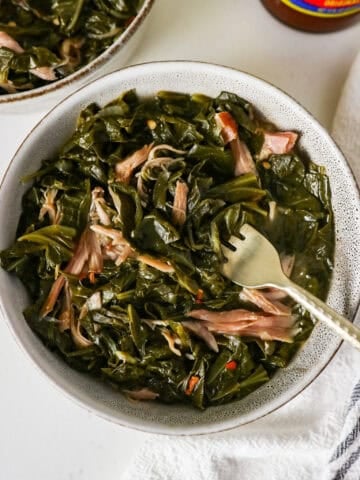 Overhead view of a bowl full of collard greens with smoked turkey and a fork lifting some out.