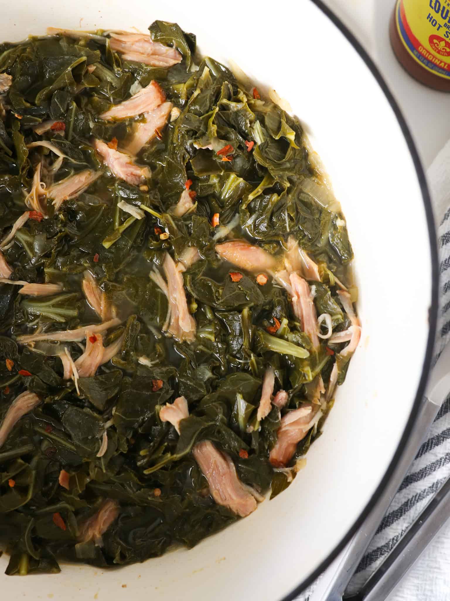 Overhead view of southern collard greens in a white dutch oven with smoked turkey meat.