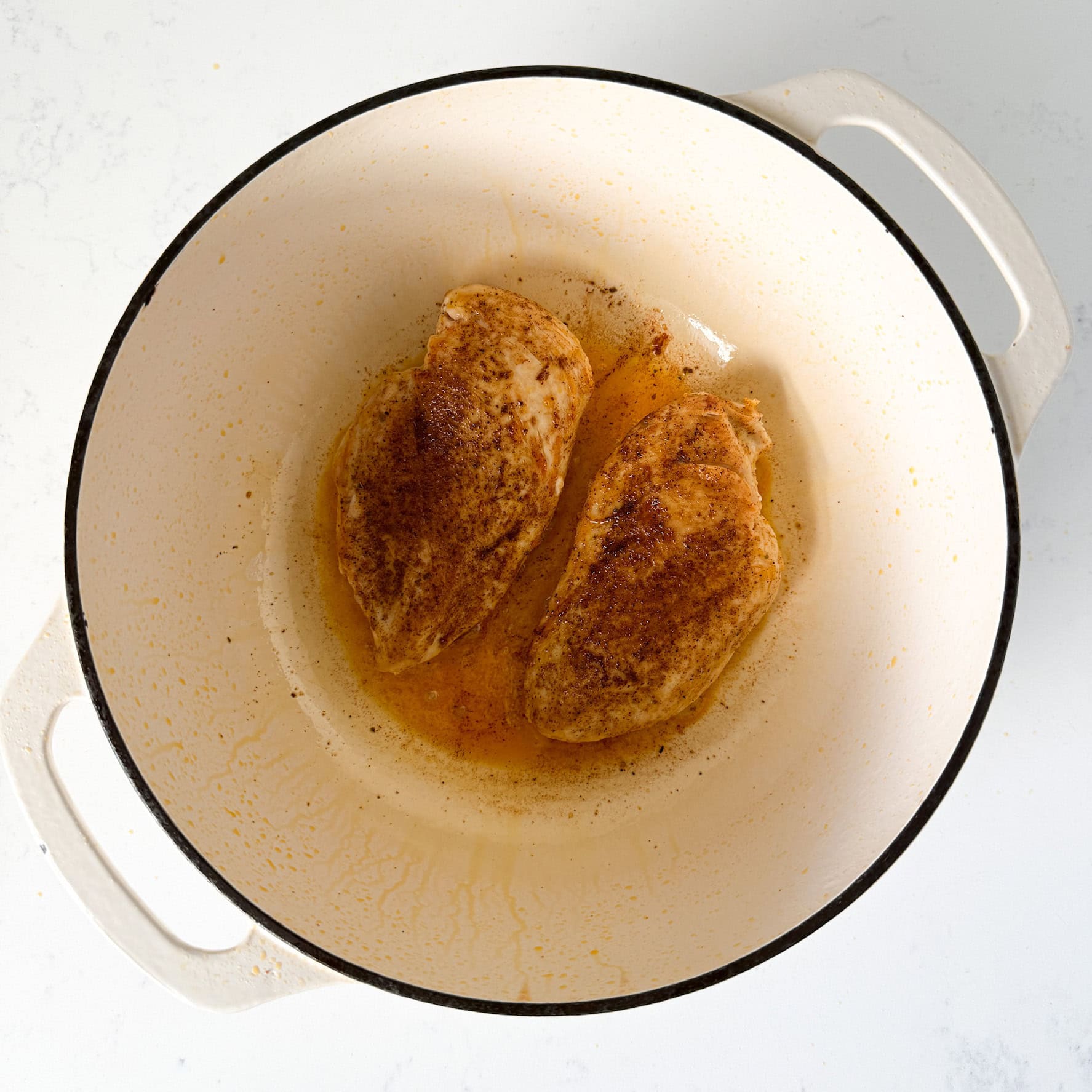 Seasoned chicken breasts seared in a white dutch oven pot.