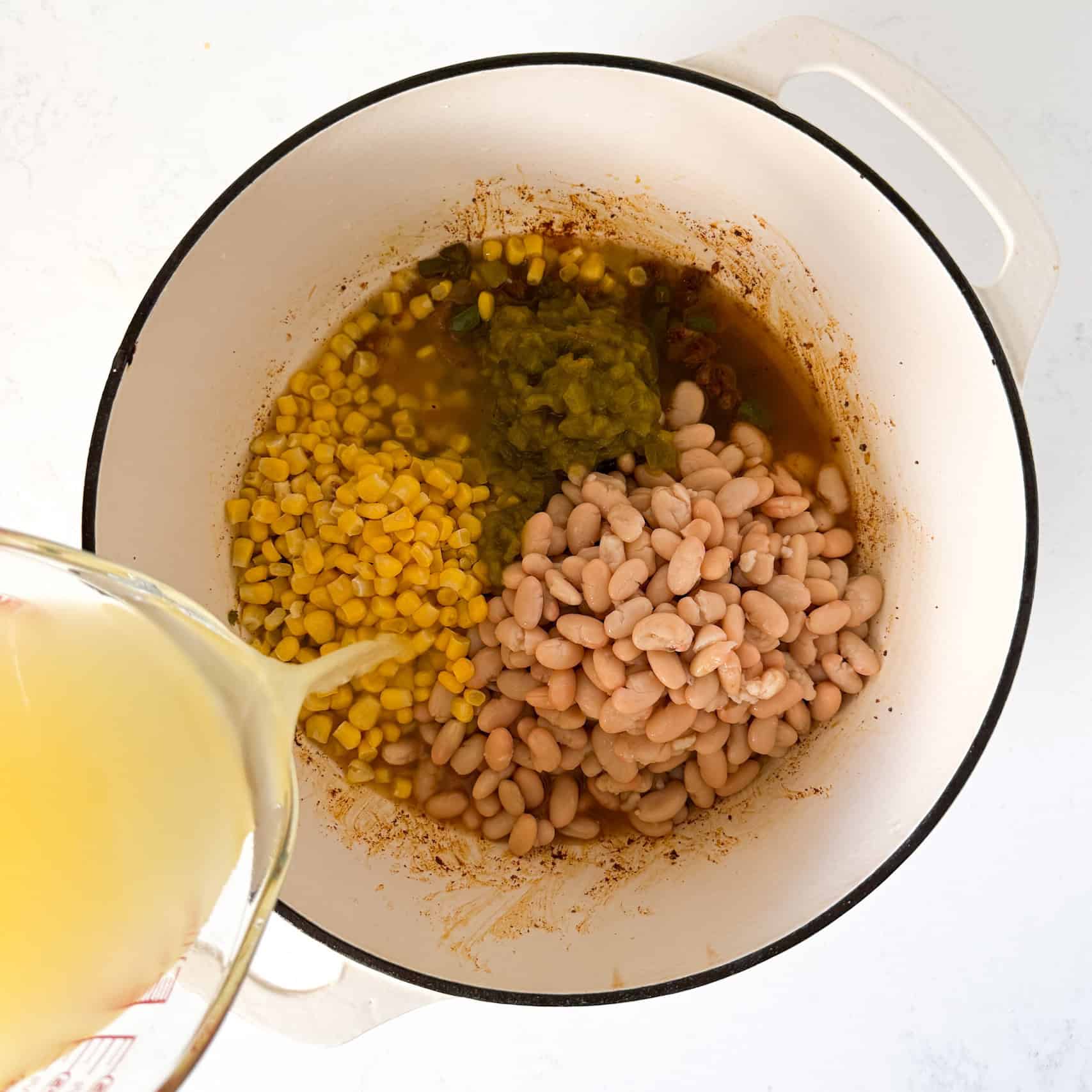 Corn, beans, green chiles, and chicken broth being added to dutch oven pot.