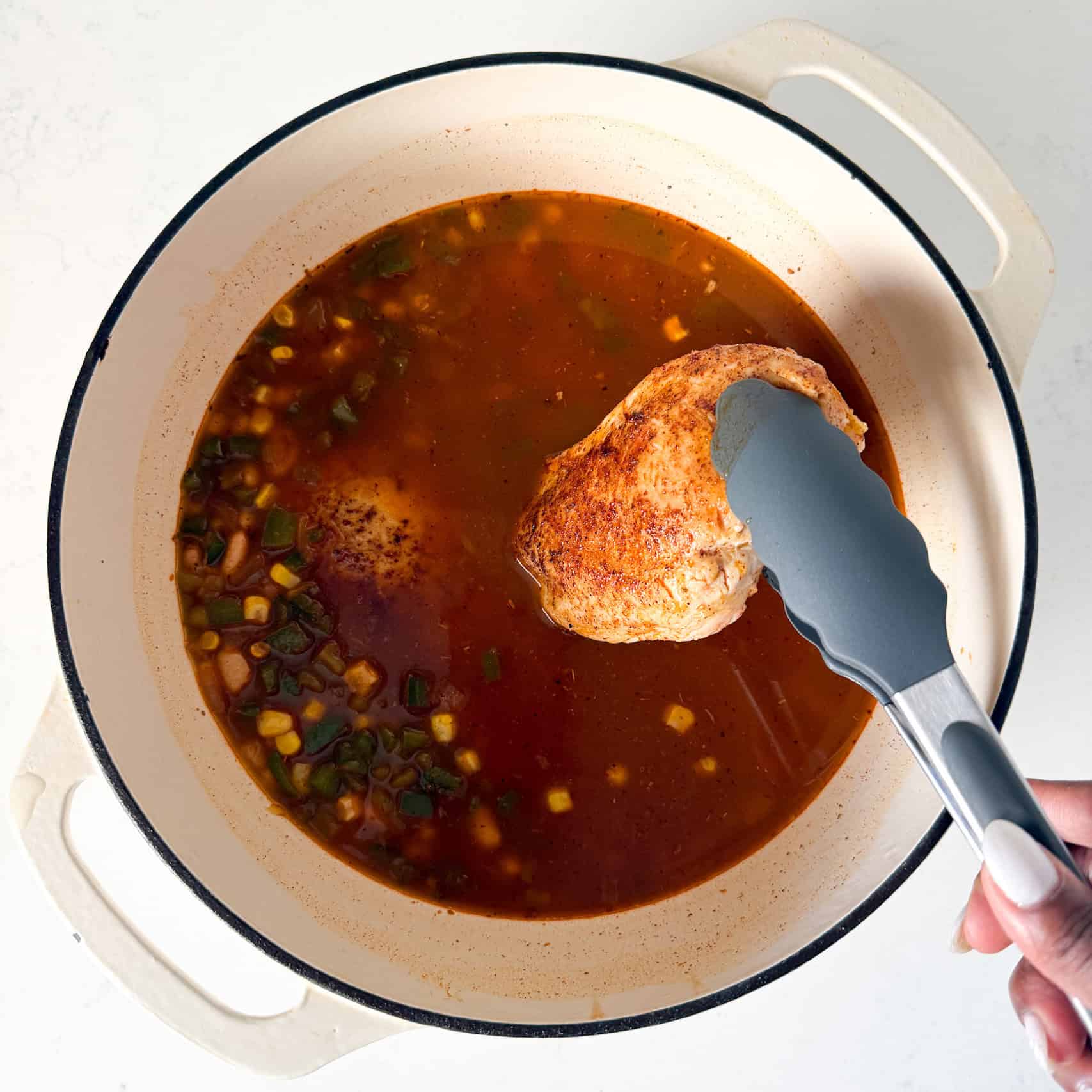 Adding seared chicken back to dutch oven pot to simmer.