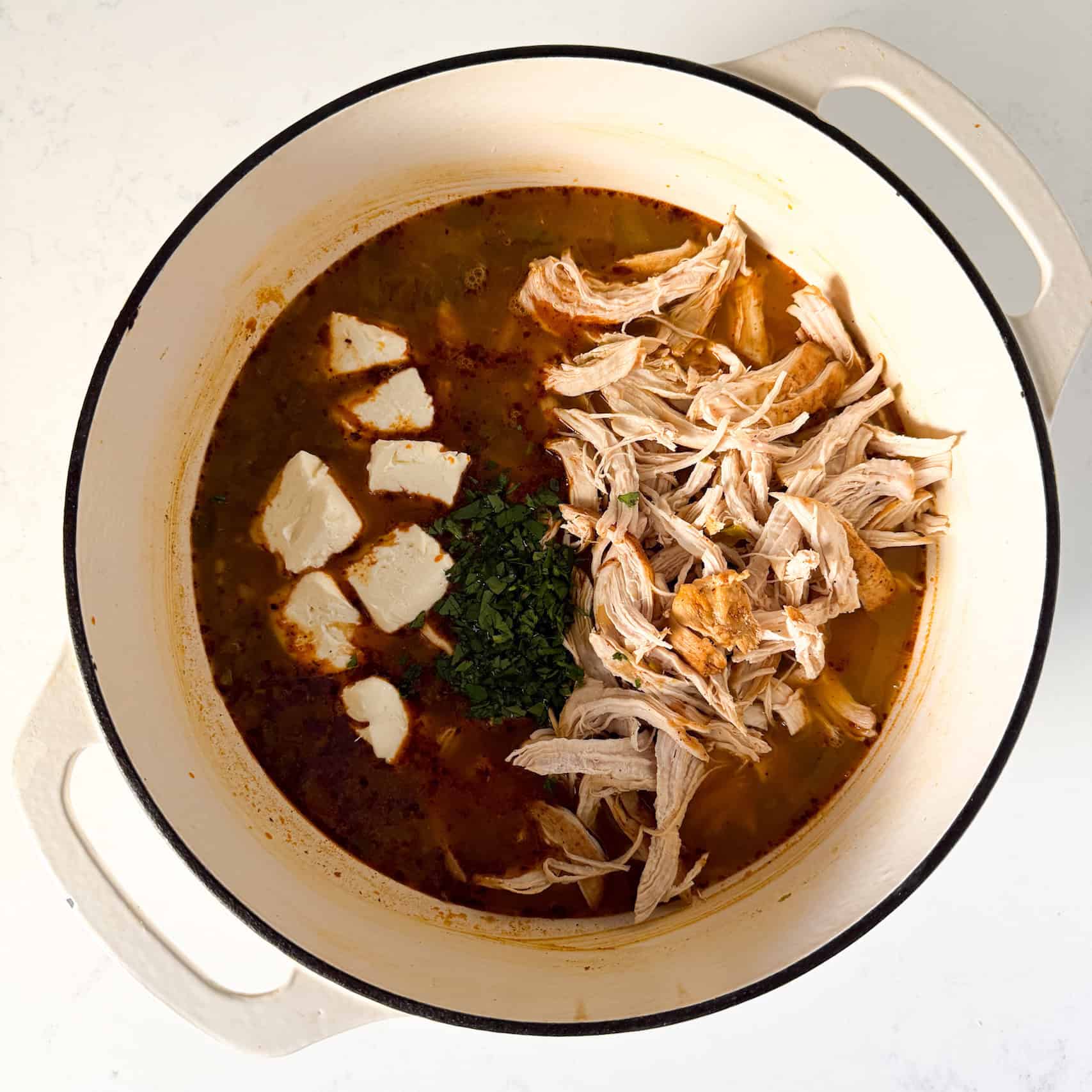 Shredded chicken, cream cheese, and chopped cilantro being added to dutch oven pot.