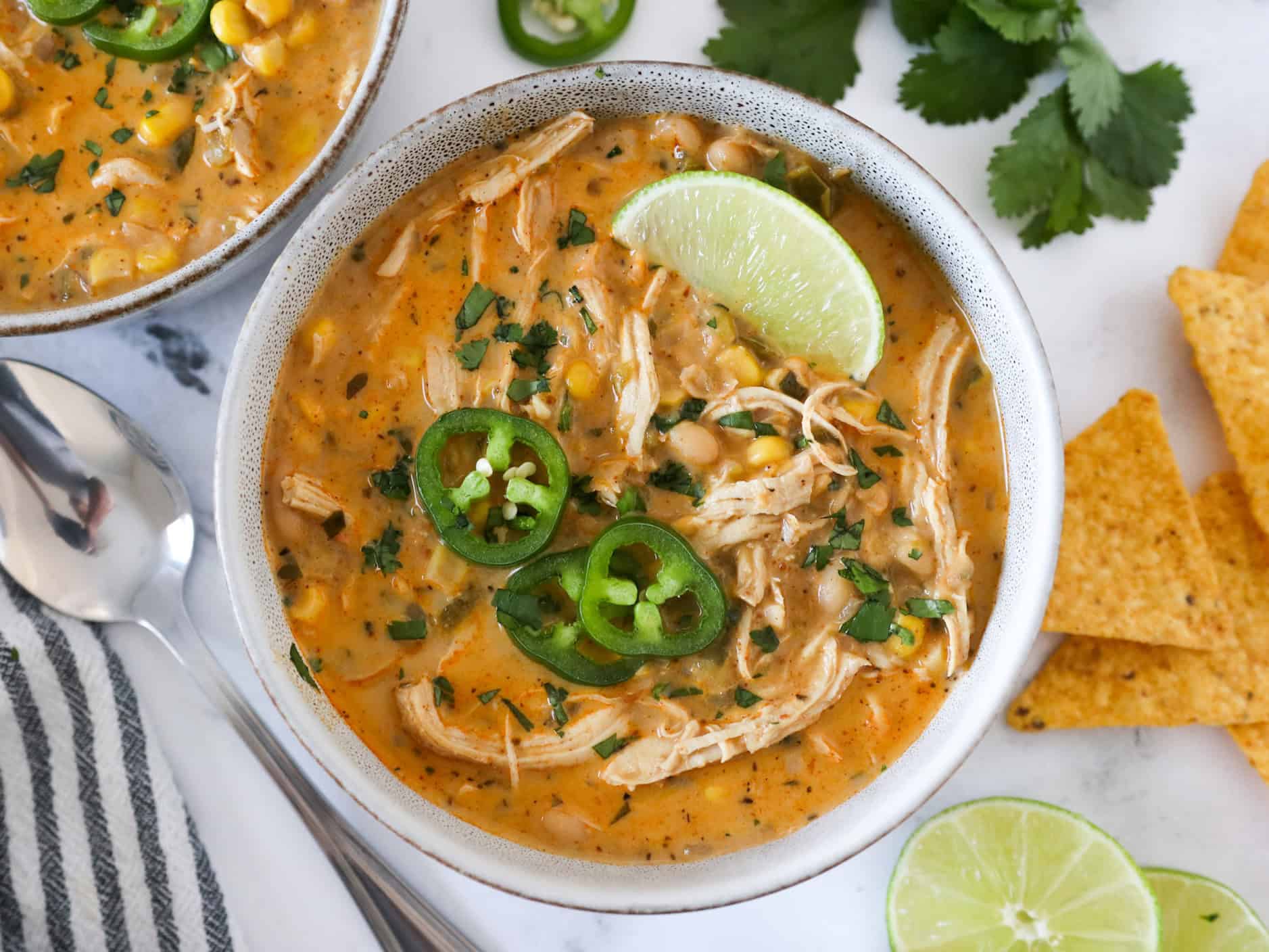Overhead view of a serving of white chicken chili in a bowl with cilantro, limes, and jalapeno on top.