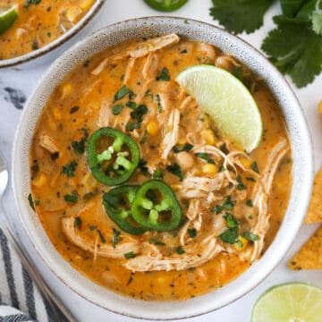 Overhead view of a serving of white chicken chili in a bowl with cilantro, limes, and jalapeno on top.