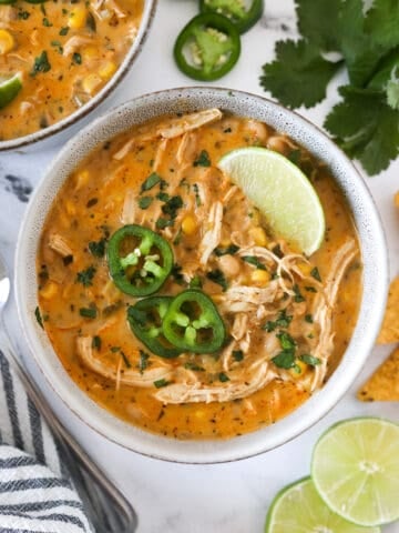 Overhead view of a serving of white chicken chili in a bowl with cilantro, limes, and jalapeno on top.