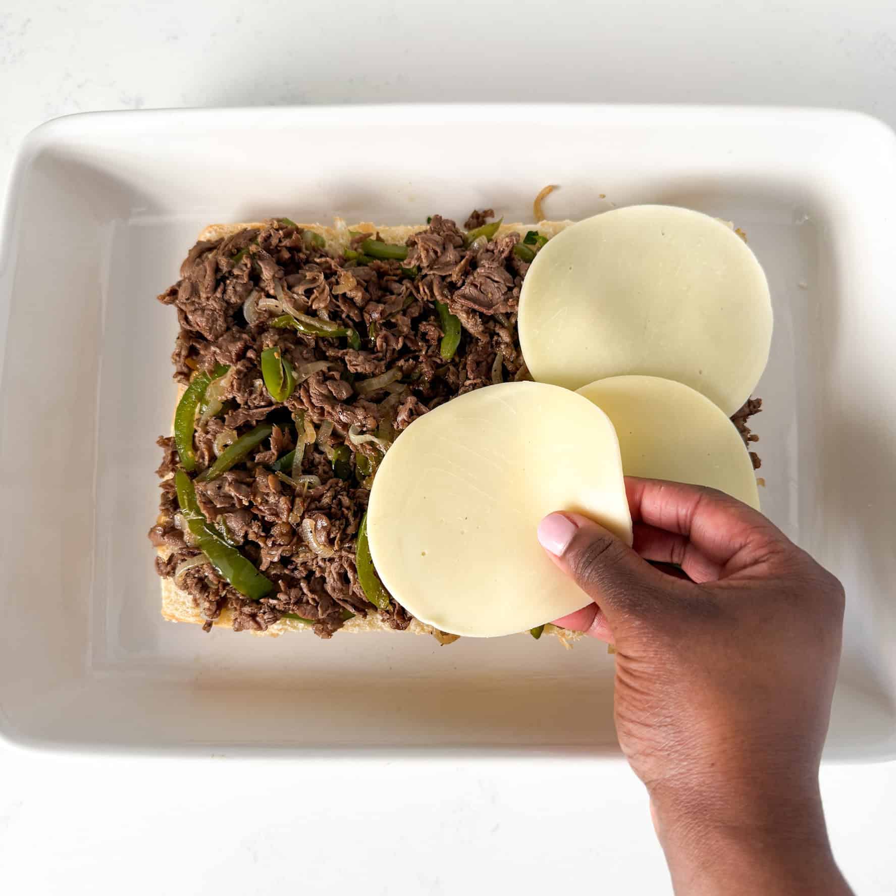Cheese being added on top of steak and rolls.