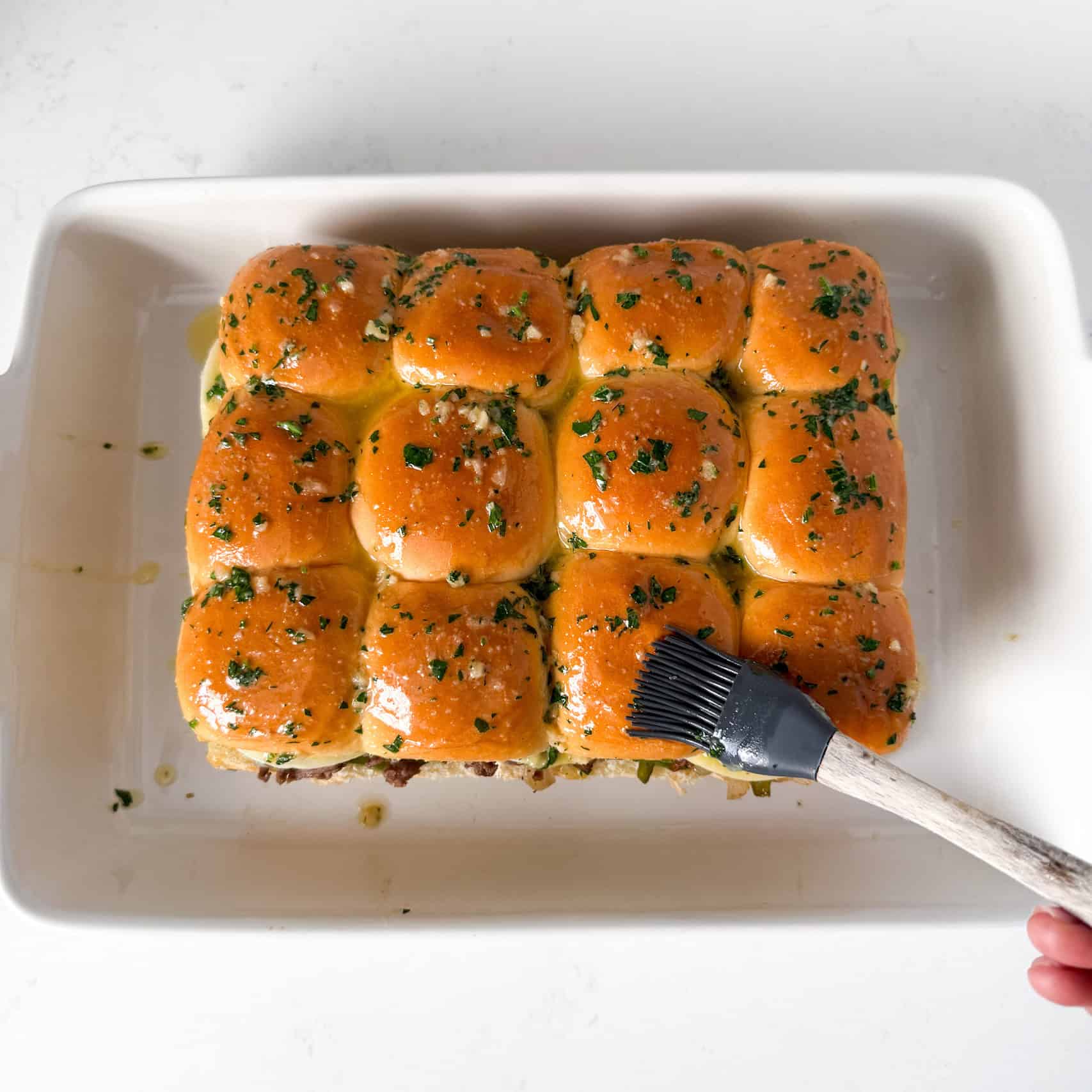 Garlic butter being brushed on top of hawaiian rolls.
