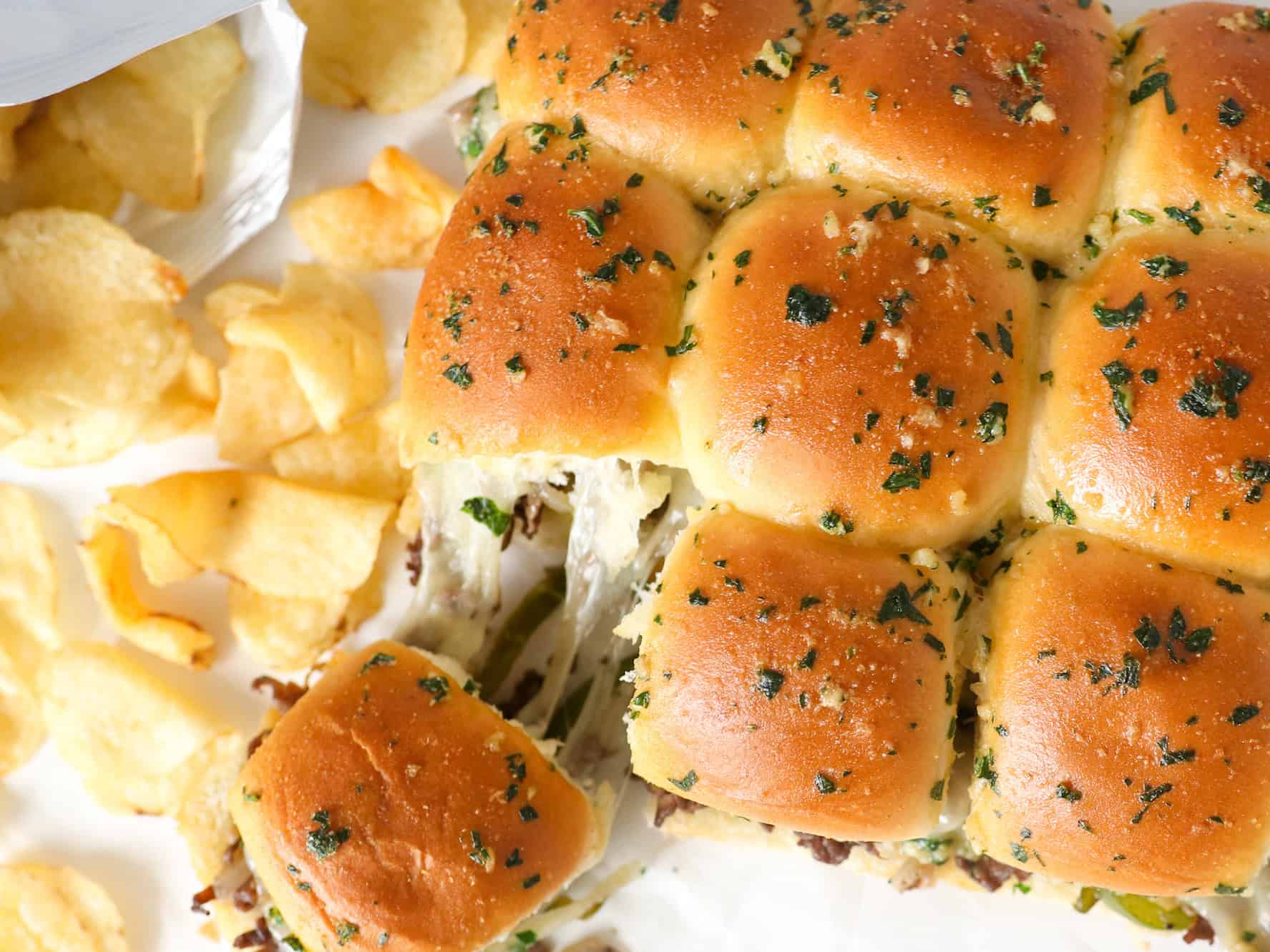 Overhead view of Philly cheesesteak sliders on parchment paper with chips on the side.