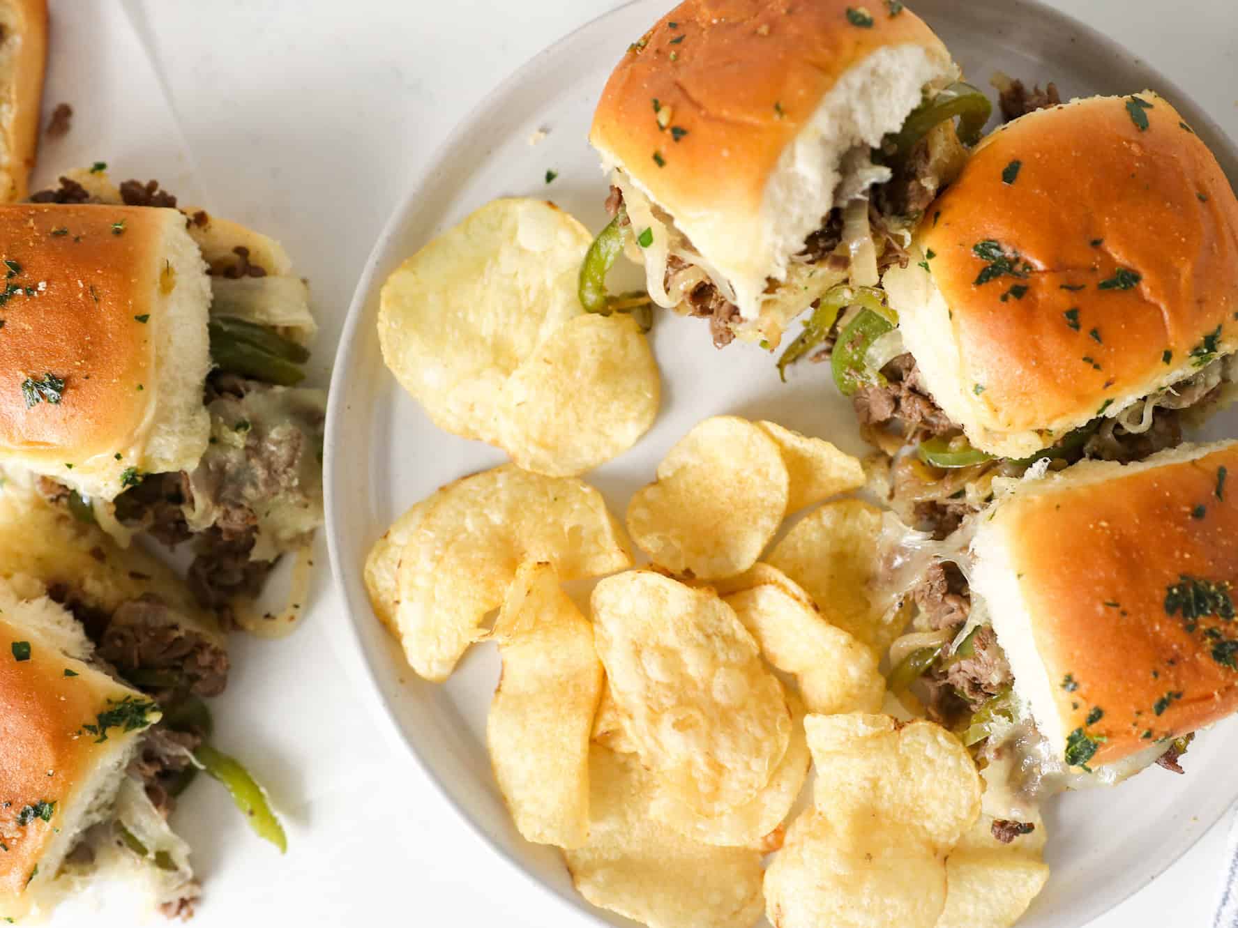 Philly cheesesteak sliders on a plate with chips on the side.