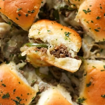 Overhead close up view of philly cheesesteak sliders with one slider turned on its side.